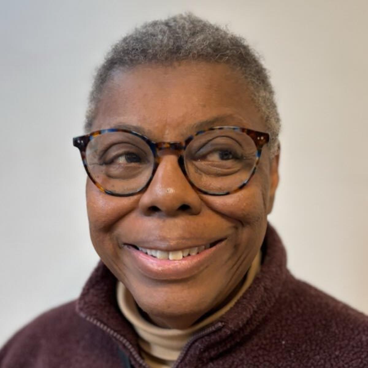 Head and shoulders of a smiling Black woman with glasses and short grey hair is looking off to the right. It's Ernie Buscemi from Morningside Meeting.